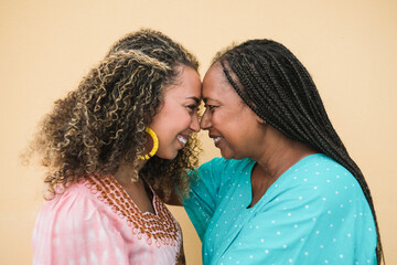 Happy african mother and adult daughter having tender moment together while wearing traditional...