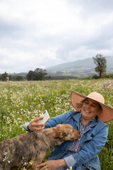 Elderly woman smiling with her dog, taking a picture in a flowery field