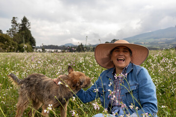 A mature woman smiling with her companion dog by her side. She is casually dressed for a walk and relaxation in the countryside