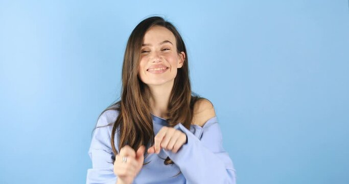 Beautiful cute young woman posing isolated on blue background in studio. People lifestyle concept. Look camera send blow air kiss showing shape heart with hands.