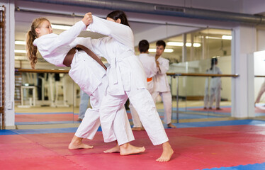 Pair of teenager girls wearing kimono practicing new karate moves during training in gym