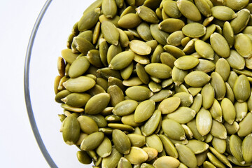 Organic green pumpkin seeds (hulled) in a glass saucer on a white background