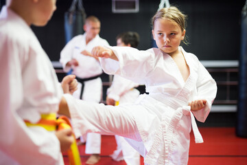 Young girls and boys in kimono and belts sparring during karate training.