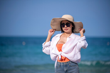 Portrait beautiful Asian woman wearing ,white t-shirt, sunglasses and straw hat at beach on vacation looking away while enjoying sea breeze is summer vacation concept.