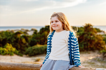 Adorable happy smiling little girl on beach vacation at sunset. Handsome cute preschool child with long blond hairs having fun on family vacations.