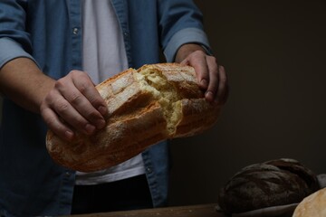 Man breaking loaf of fresh bread at wooden table, closeup