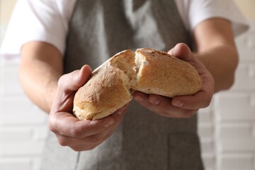 Man breaking loaf of fresh bread near white brick wall, closeup