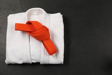 Orange karate belt and white kimono on gray background, top view. Space for text
