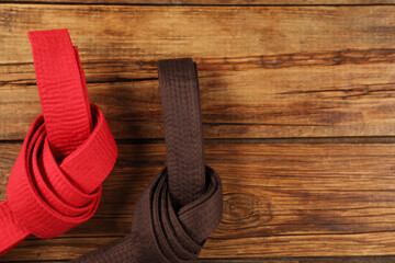 Red and brown karate belts on wooden background, flat lay