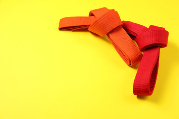 Red and orange karate belts on yellow background, space for text