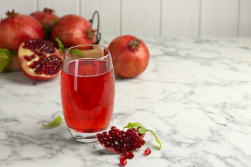 Tasty pomegranate juice in glass and fresh fruits on white marble table. Space for text
