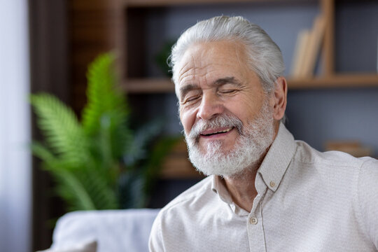 Close-up photo of an older smiling gray-haired man at home, resting with his eyes closed and thoughtfully dreaming