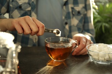 Woman adding sugar cube into cup of tea at dark table, closeup