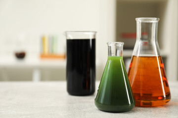 Flasks and beaker with different types of crude oil on light grey table, space for text