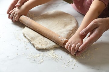 Father and child rolling raw dough at white table, closeup