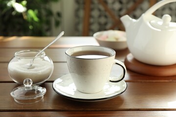 Cup of aromatic tea and sugar on wooden table