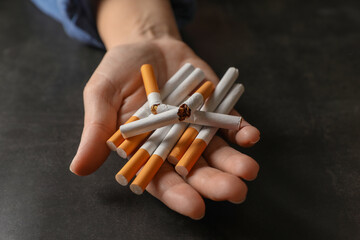 Stop smoking. Woman holding whole and broken cigarettes at black table, closeup