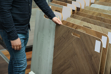 Man choosing wooden flooring among different samples in shop, closeup