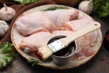 Plate with fresh marinade, raw chicken and basting brush on wooden table, closeup