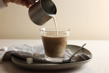 Pouring milk into cup with coffee on white wooden table, closeup