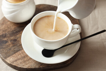 Pouring milk into cup with tea on light table, closeup