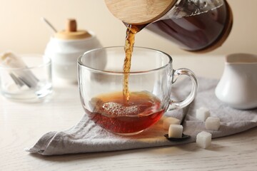 Pouring warm tea into cup on white wooden table, closeup