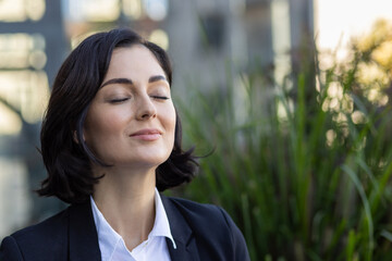 Close-up photo of a young business woman standing outside on the street in a suit with her eyes closed and resting, thoughtfully taking deep breaths - Powered by Adobe