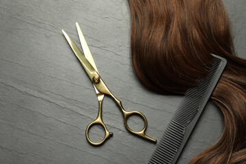 Professional hairdresser scissors and comb with brown hair strand on dark grey table, top view