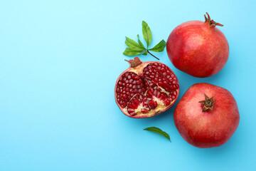 Fresh pomegranates and green leaves on light blue background, flat lay. Space for text