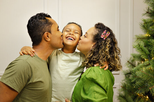 Familia Parda com tra&ccedil;os brasileiros com homem, mulher e um menino crian&ccedil;a, em uma sala com uma decora&ccedil;&atilde;o de natal na cor verde.