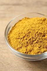 Curry powder in bowl on wooden table, closeup