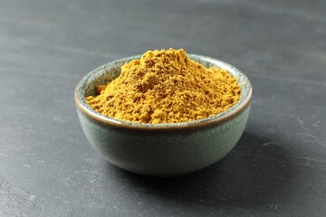 Dry curry powder in bowl on dark table, closeup