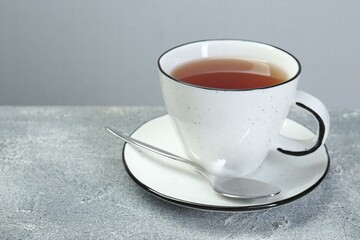 Aromatic tea in cup and spoon on grey table. Space for text