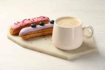 Cup of coffee and delicious eclairs covered with glaze on white wooden table