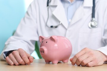 Doctor with piggy bank at wooden table, closeup