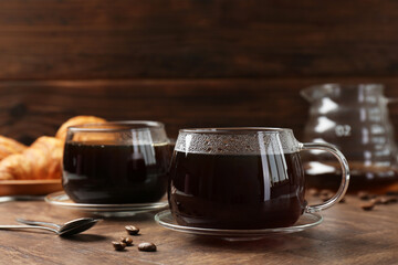 Hot coffee in glass cups, spoons and beans on wooden table, closeup