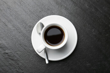 Hot coffee in cup, spoon and saucer on dark textured table, top view
