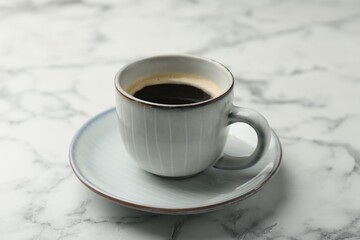 Tasty coffee in cup and saucer on white marble table, closeup