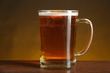 Mug with fresh beer on wooden table against dark background, closeup