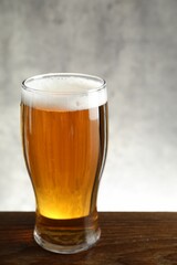 Glass with fresh beer on wooden table against light background