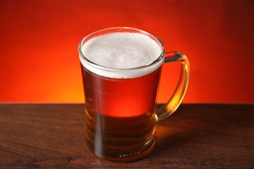 Mug with fresh beer on wooden table against red background, closeup