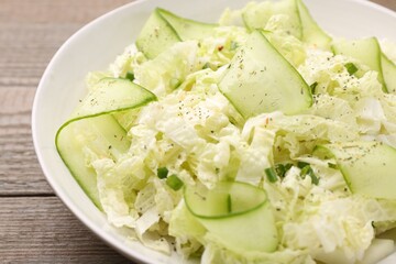 Tasty salad with Chinese cabbage, cucumber and green onion in bowl on wooden table, closeup