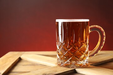 Mug with fresh beer on wooden crate against color background. Space for text