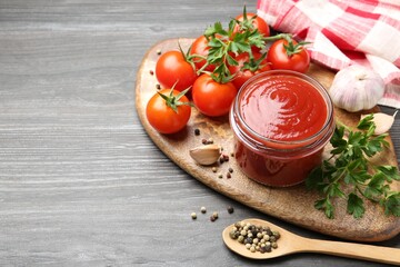 Tasty ketchup, fresh tomatoes, parsley and spices on grey wooden table, space for text
