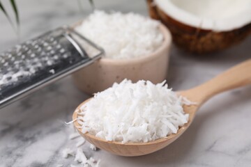 Fototapeta na wymiar Coconut flakes in wooden spoon and grater on white marble table, closeup