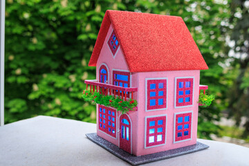 Against a background of green trees, a pink house with a red roof and blue light in the windows