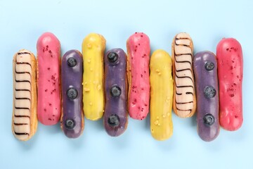 Delicious eclairs covered with glaze on light blue background, top view
