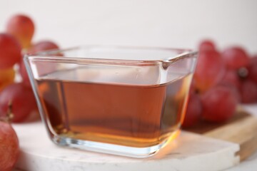 Wine vinegar in glass bowl and grapes on table, closeup