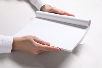 Woman holding notebook with blank pages at white table, closeup. Mockup for design