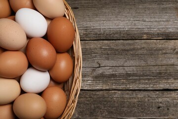 Fresh chicken eggs in wicker basket on wooden table, top view. Space for text